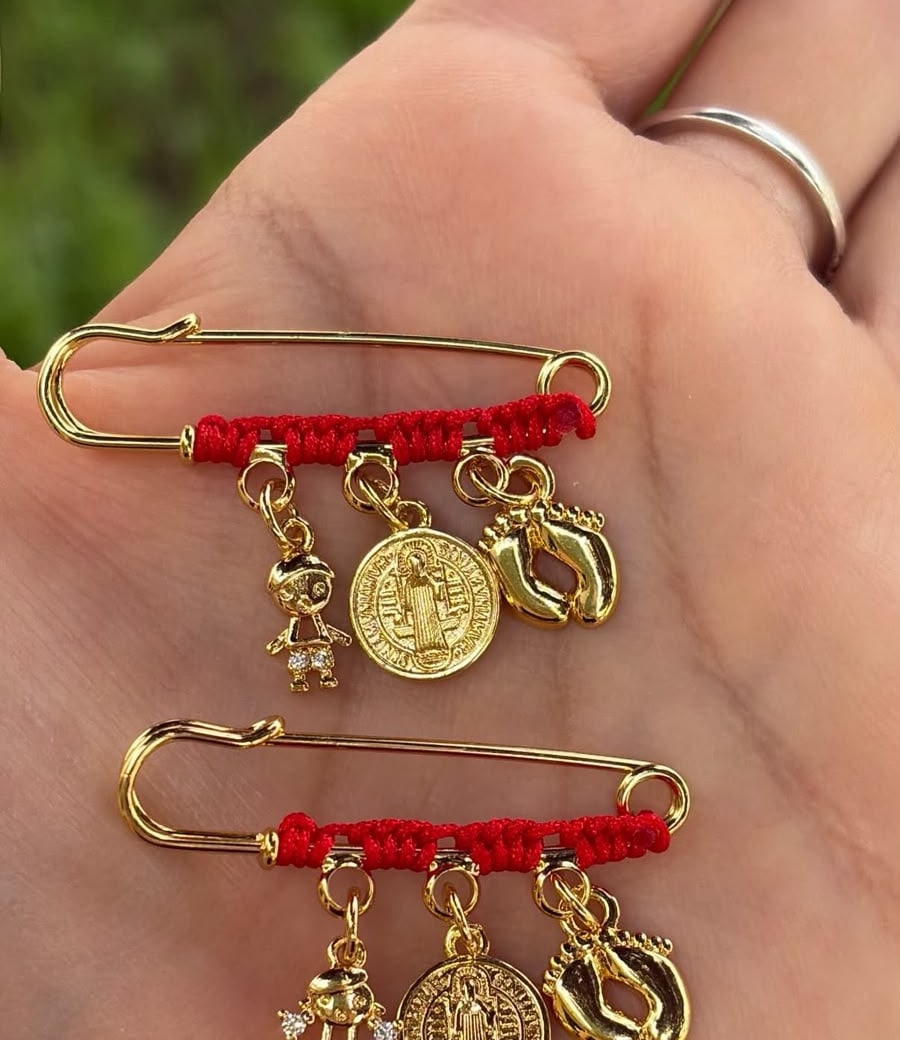 Dos prendedores con hilo rojo, figura de niño o niña, medalla y pies de bebé.
