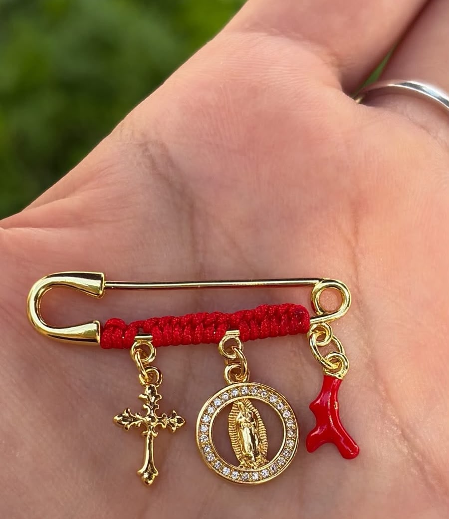 Prendedor con hilo rojo, cruz, medalla de la Virgen y cuerno rojo.